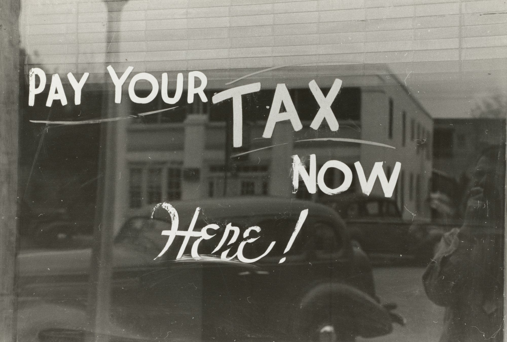 Hand-lettered sign painted on a shop window, a parked car visible through the glass